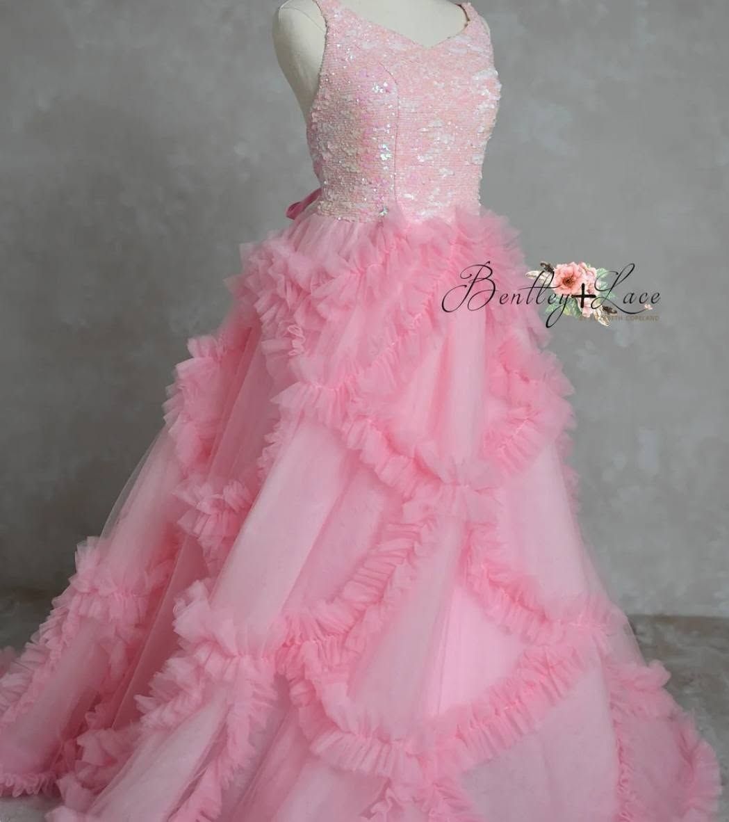 Young dancer twirls in elaborate pink ruffled ball gown against floral backdrop.