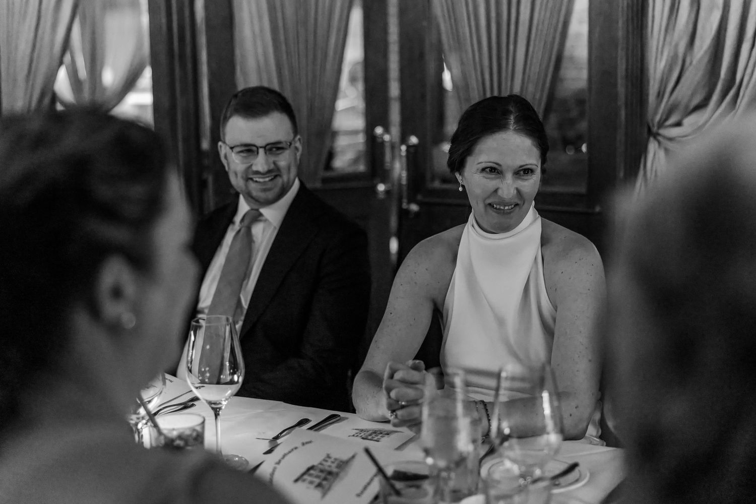 Black and white photo of a smiling couple seated at an elegant dining table during a formal event.
