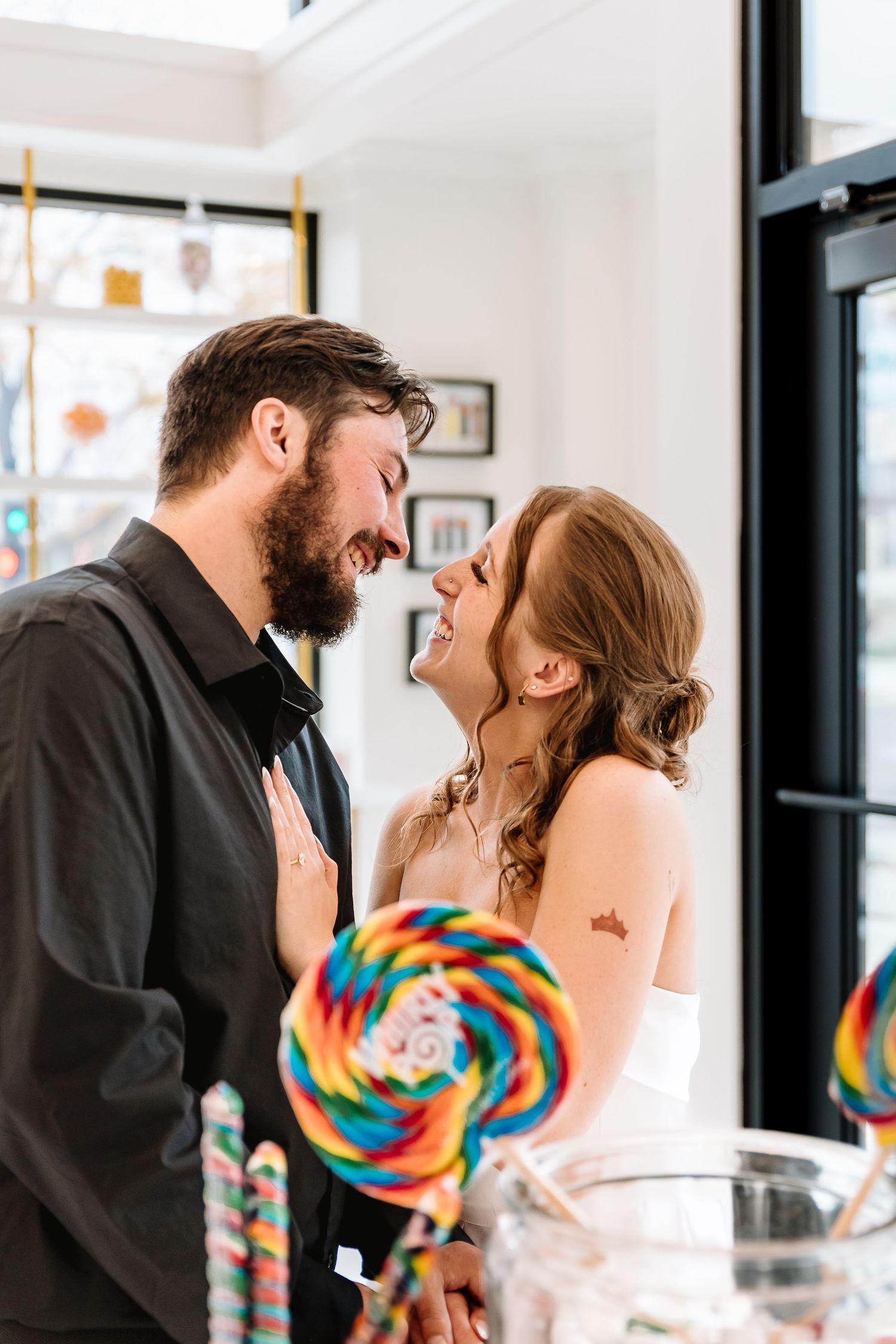 A joyful couple sharing a romantic moment at a colorful candy bar, with rainbow lollipops in the foreground.