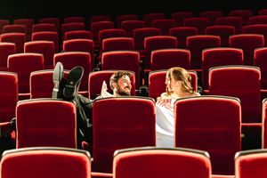 Couple relaxing in empty red theater seats, smiling and talking during a private cinema screening.