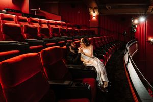 Bride and groom share a romantic moment in empty red theater seats during a cinematic wedding photo session.