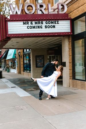 Newlyweds Mr. & Mrs. Gomez share a romantic dip kiss outside the World Theater marquee announcing their coming soon.