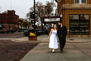 A couple walks hand-in-hand past the World Theater marquee on a brick street corner in a small town.