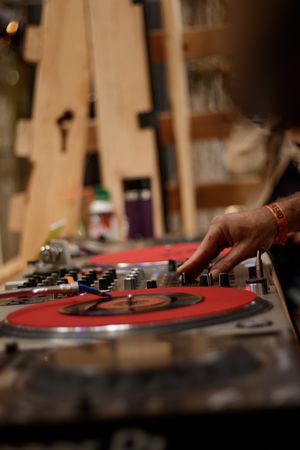 A DJ's hands adjusting controls on a mixer with red vinyl turntables in a warmly lit studio setting.
