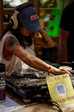 Female DJ with tattoos and headphones operates Pioneer DJ turntables at Center for Cassette Studies event.
