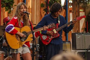 Two young musicians performing live, girl singing and playing acoustic guitar, boy playing red electric guitar.