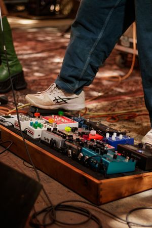 Musician stepping on guitar effects pedal board with multiple colorful pedals on a wooden tray during a live session.