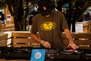 DJ performing outdoors on turntables wearing a Wu-Tang Clan shirt and black cap at a PDX event.