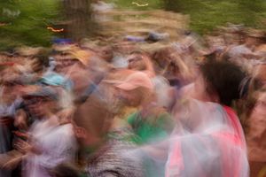 Blurry motion shot of a large crowd of people gathered outdoors at a festival or concert.