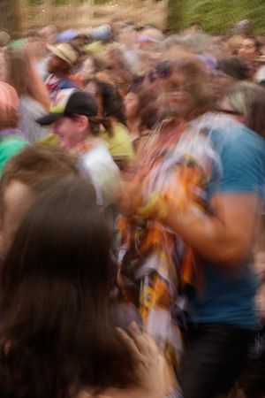 Blurred motion photo of a large crowd of people dancing and celebrating at an outdoor music festival.
