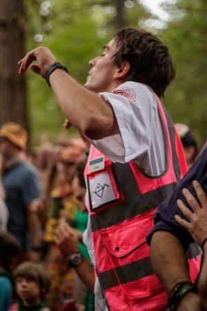 A festival security worker in a pink high-visibility vest points while managing crowds at an outdoor event.