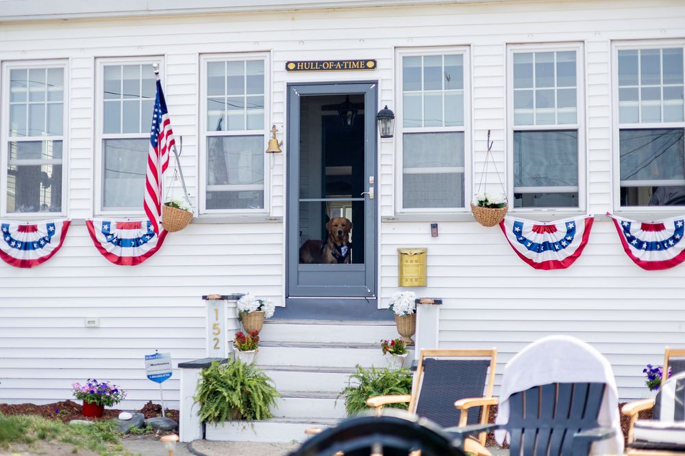 White house decorated with patriotic red, white, and blue bunting, American flag, and rocking chairs for Fourth of July.
