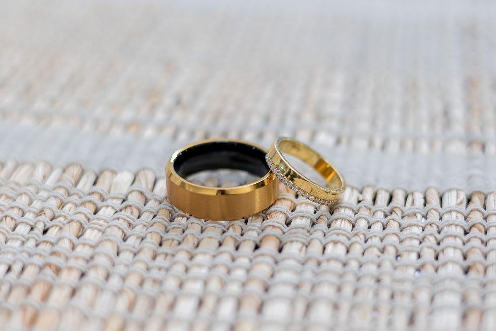 Two gold wedding bands resting on a woven white textile surface, one plain and one with diamond accents.