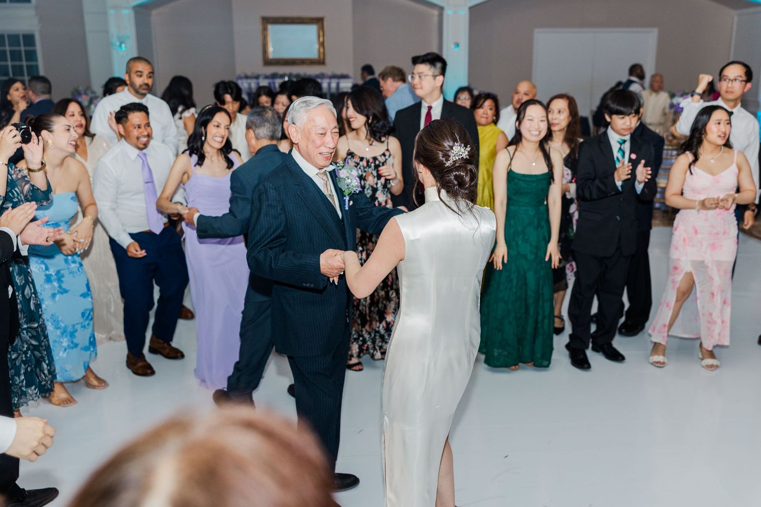 Elderly man and bride share a father-daughter dance at a wedding reception with guests watching in the background.