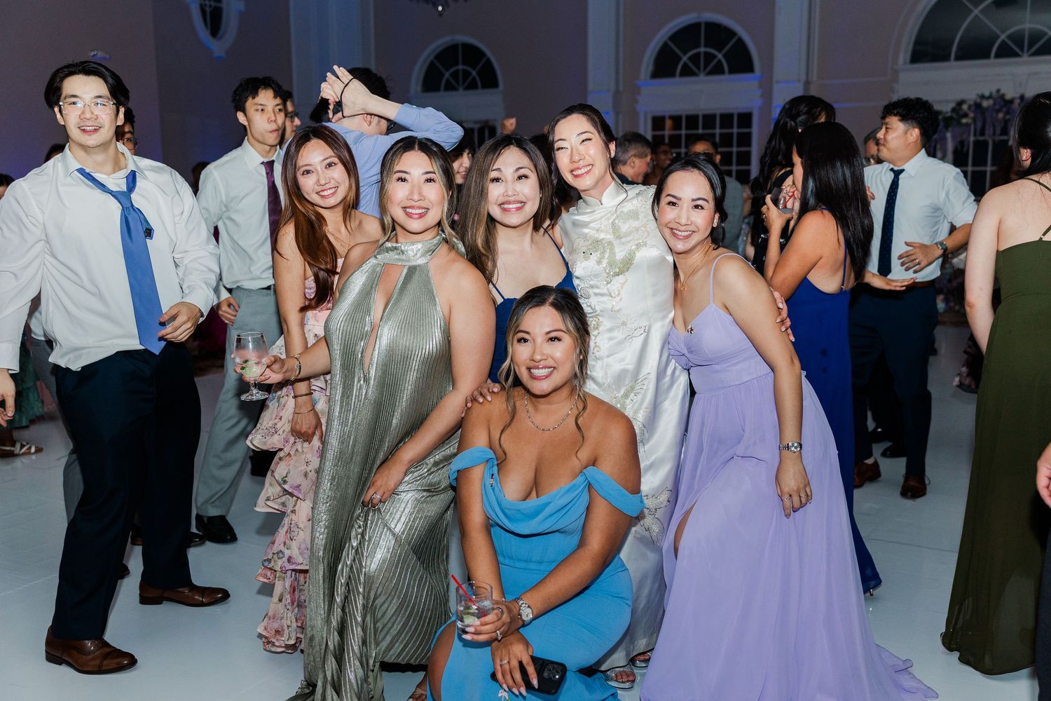 Group of elegantly dressed friends posing and dancing together at a formal wedding reception celebration.