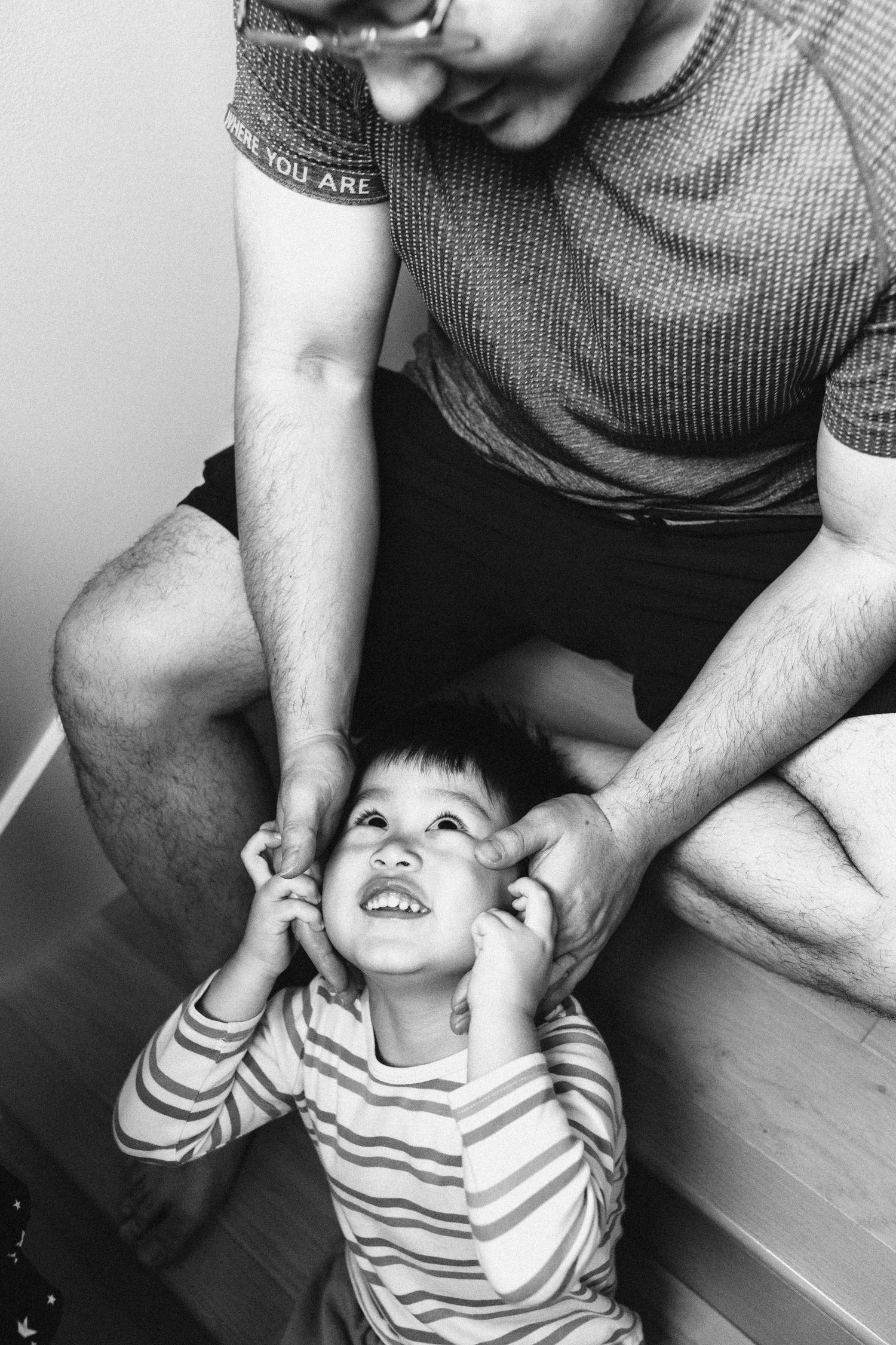 Black and white photo of a father playfully cupping the face of his laughing toddler son.