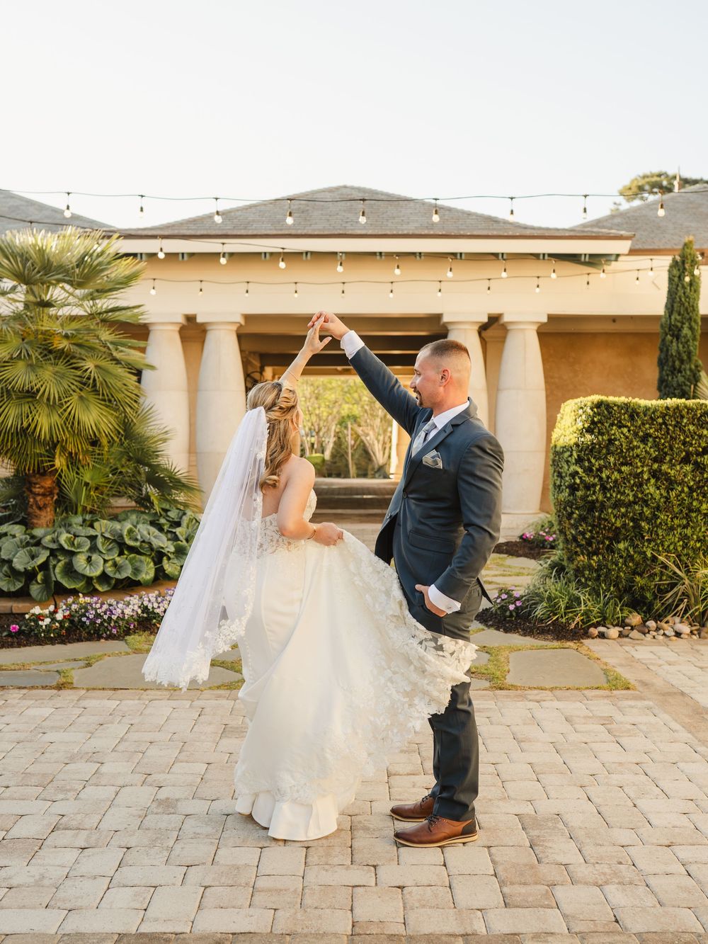 Bride and groom dancing outdoors on a brick patio at a wedding venue with elegant columns and string lights.