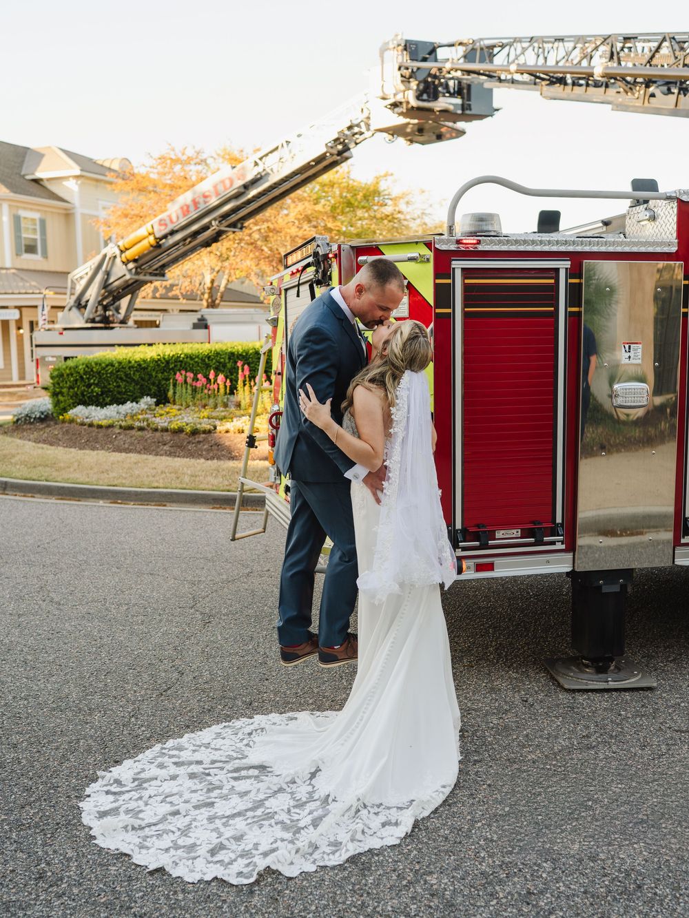 Bride and groom sharing a romantic kiss in front of a red fire truck on their wedding day.