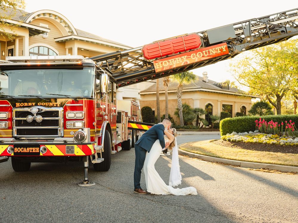 Bride and groom share a romantic kiss beside a Horry County fire truck at their outdoor wedding venue.