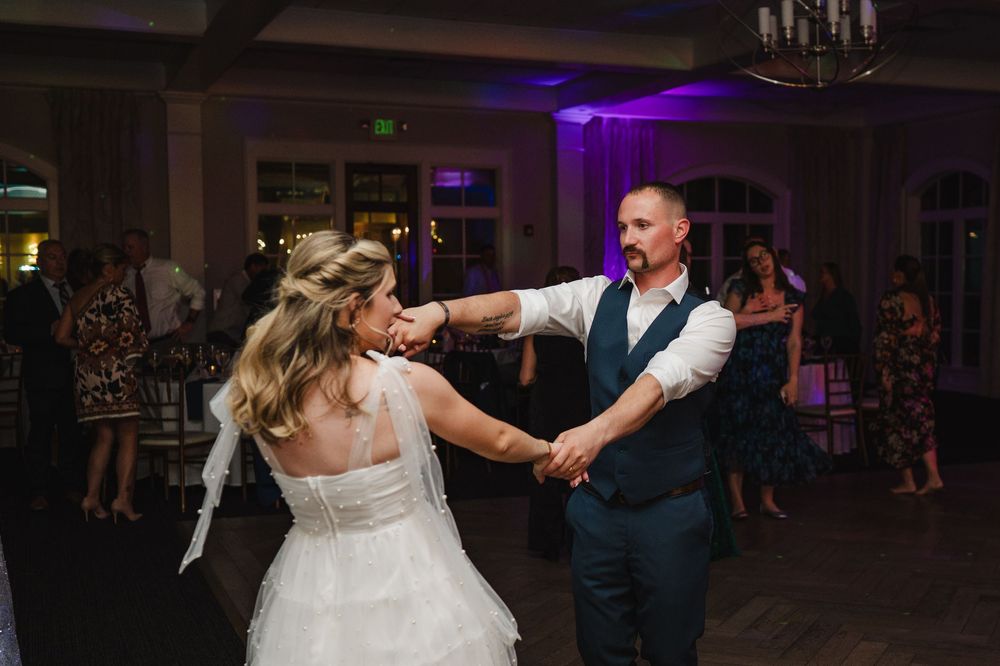 Bride and groom sharing a first dance at their wedding reception with purple lighting and guests in background.