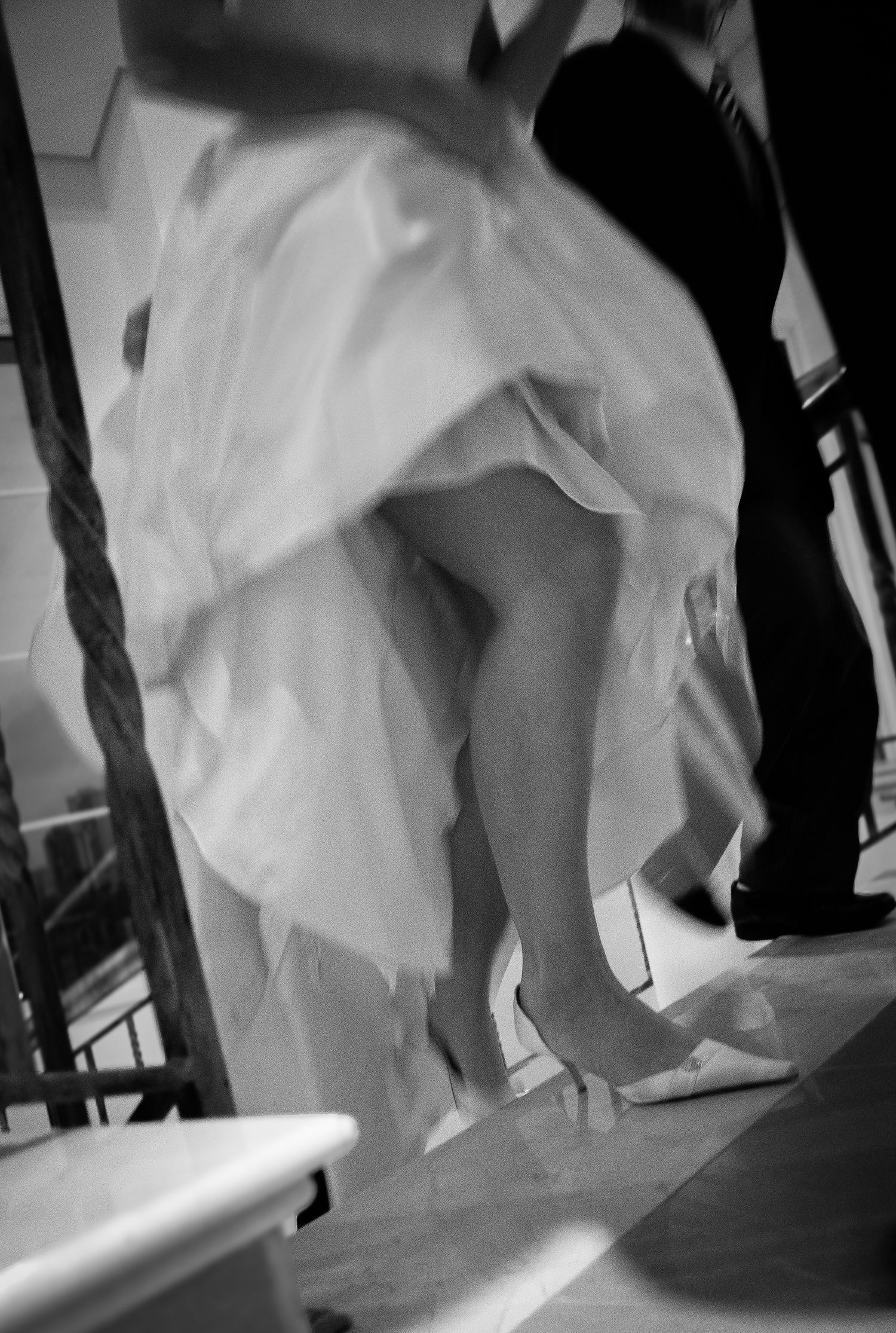 Black and white motion-blur photo of bride's white gown and heels during wedding reception dancing.