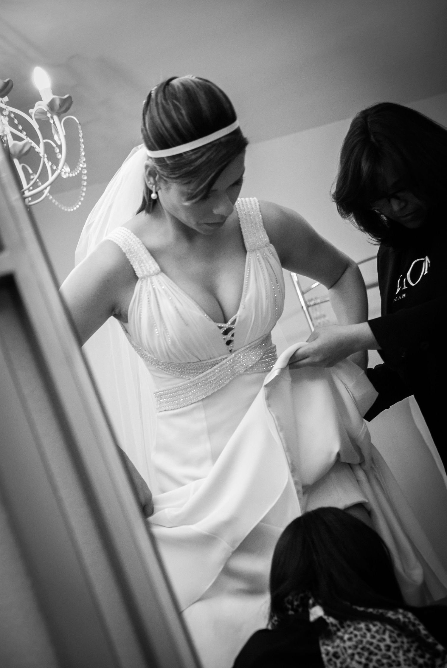 Bride in elegant white halter wedding dress being helped by attendants during bridal preparation.
