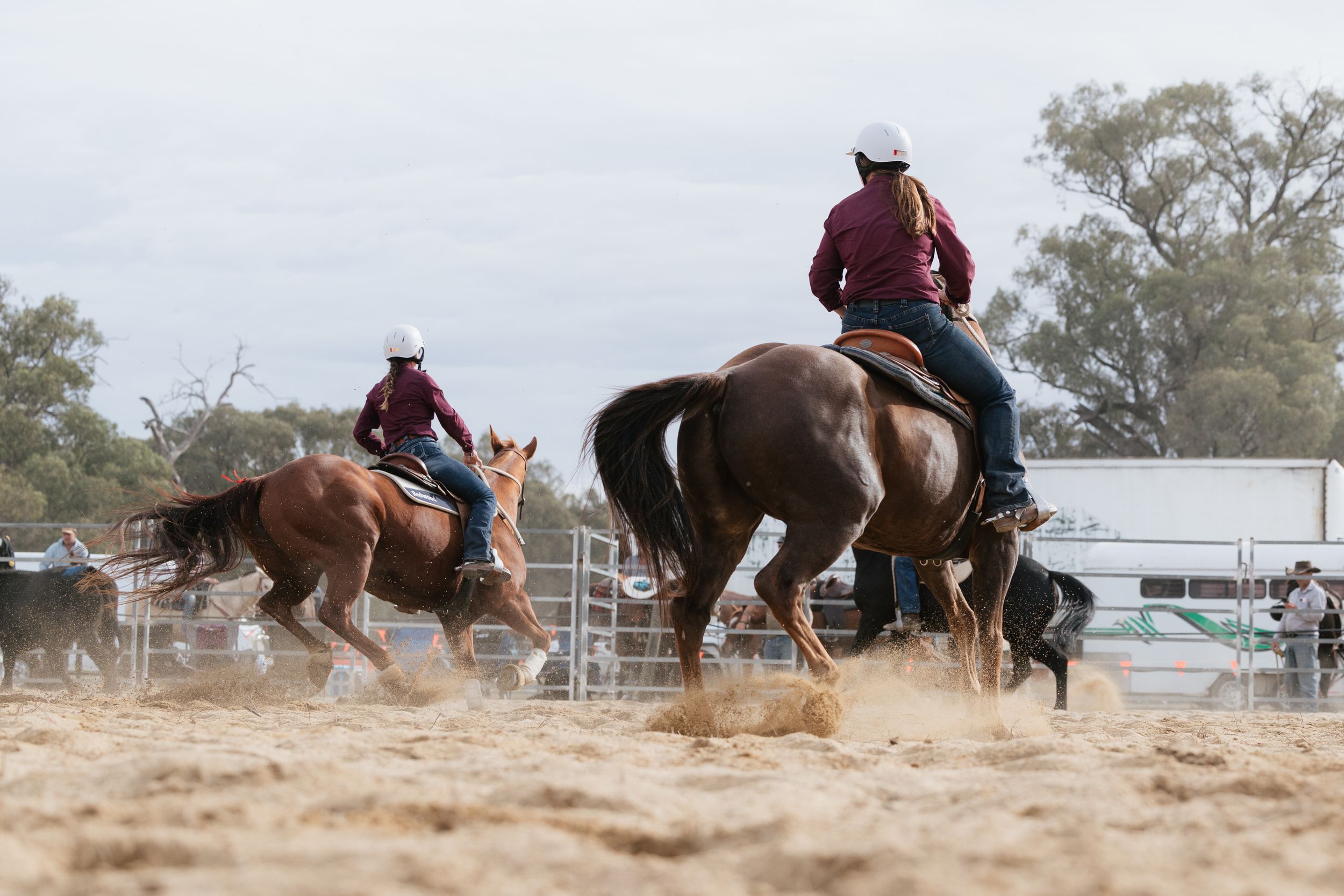 Cowboys on horseback compete in team roping event at outdoor rodeo arena in dusty sandy ring.