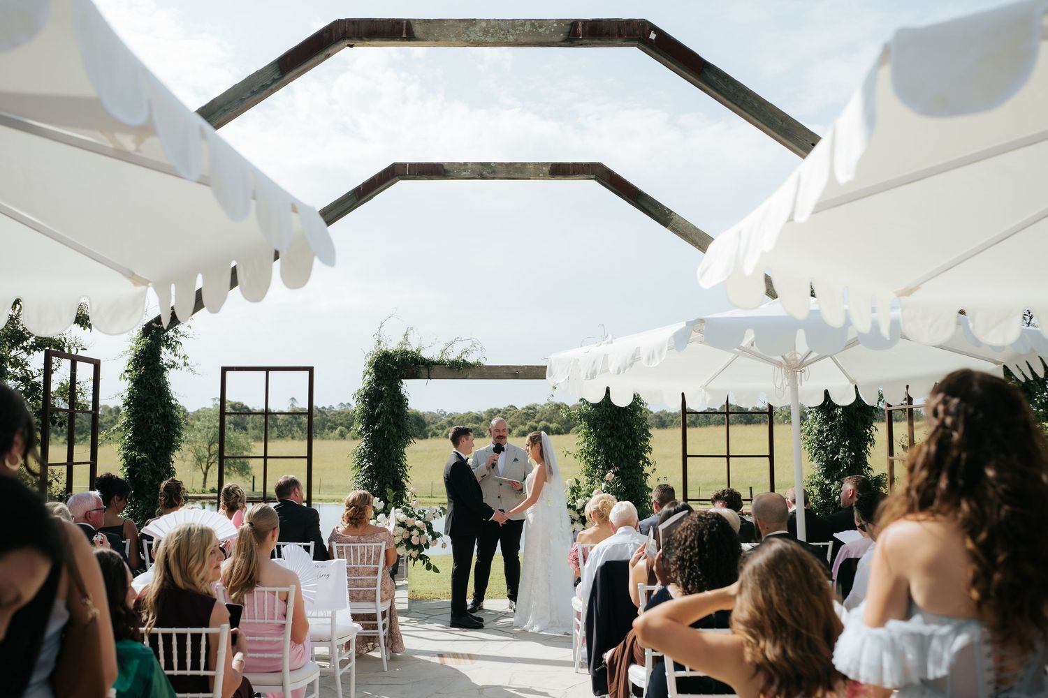 Couple embracing in wedding attire by the ocean, bride in white gown with long sleeves, groom in gray suit.