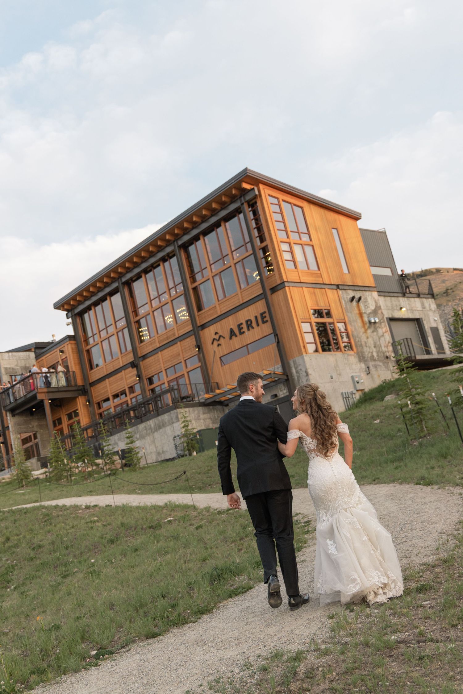 White wedding gown hanging on a hanger near a rustic wooden window with a scenic mountain forest view.