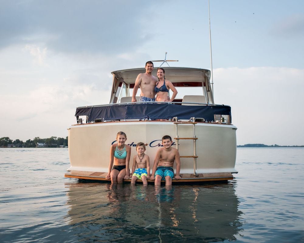 Family of five posing on and around a boat in shallow water, smiling in matching turquoise swimwear.