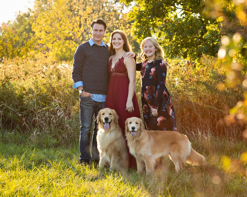 Family portrait with two golden retrievers in a sunny autumn field.