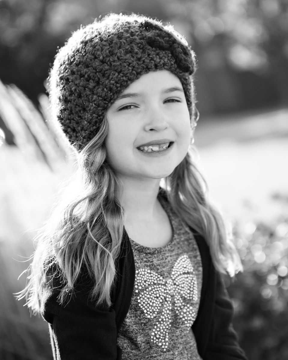 Black and white portrait of a smiling girl in a knit hat outdoors.