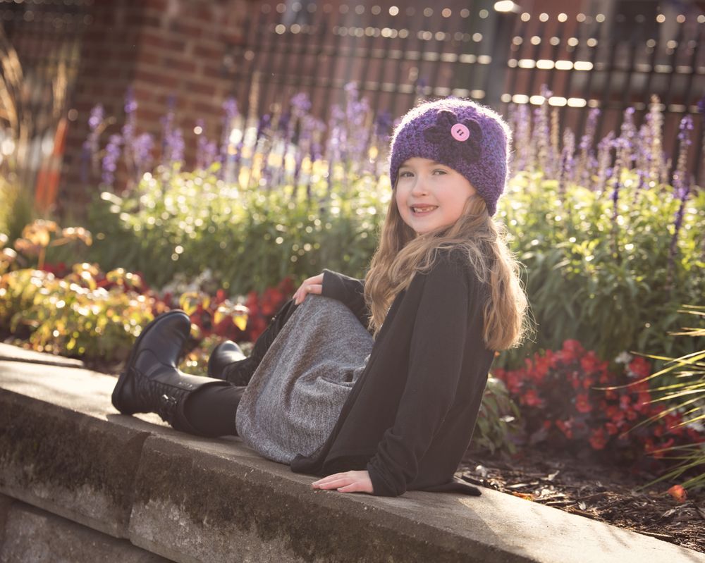 Young girl in purple hat sitting on a stone wall with a backpack.