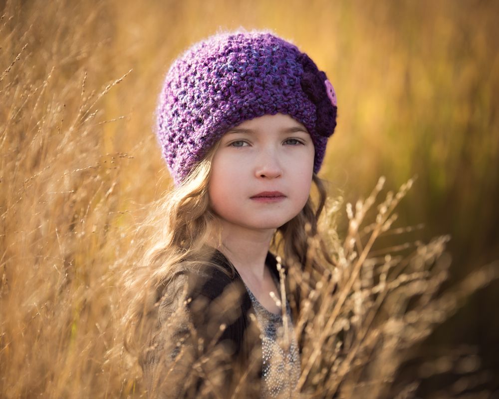 Young girl in purple crochet hat posing in a golden wheat field.