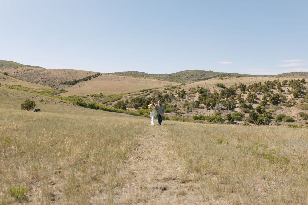 Bride and groom walking hand in hand through scenic green rolling hills on their wedding day.