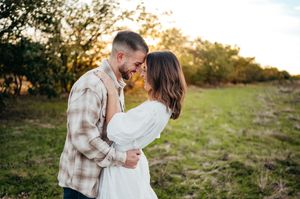 Romantic couple embracing and touching foreheads in a green field at warm sunset.
