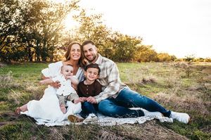 Family of four sitting on a blanket in a golden field at sunset, smiling warmly together.