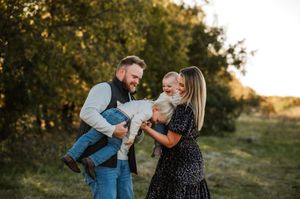 A joyful couple shares a tender moment with their laughing baby in a golden hour field.