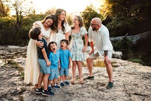 Joyful extended family laughing together on sun-drenched rocks surrounded by lush greenery.