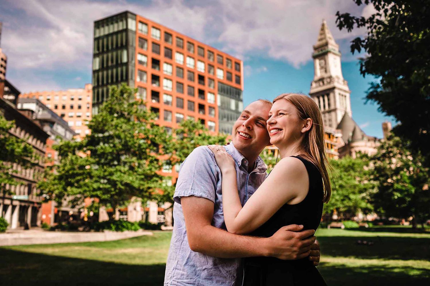 Engaged couple embracing with the Custom House Tower and Boston skyline behind them during their Rowes Wharf engagement session