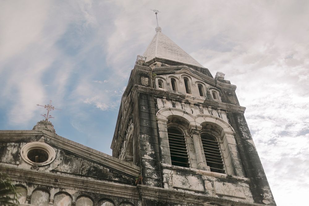 Historic stone church tower with arched windows and spire against a cloudy sky, showcasing colonial Gothic architecture.