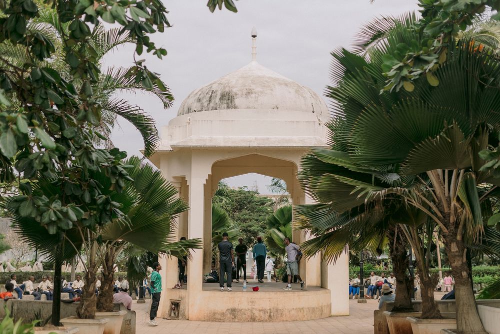 White domed marble pavilion gazebo surrounded by lush palm trees in a historic Indian garden park with visitors.