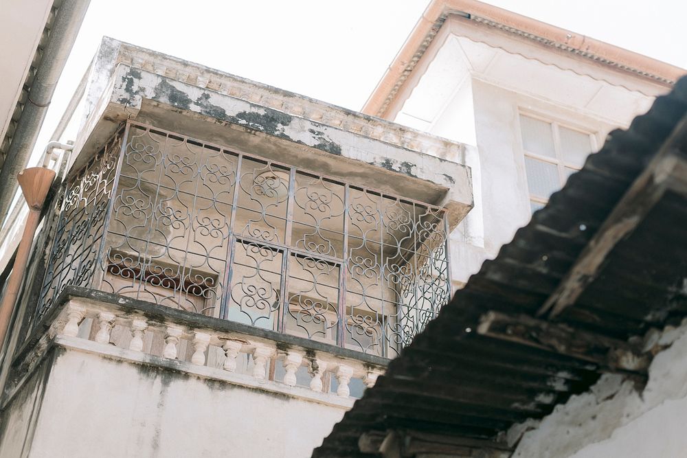 Weathered building facade with ornate wrought iron balcony and peeling white paint in an old Mediterranean town.