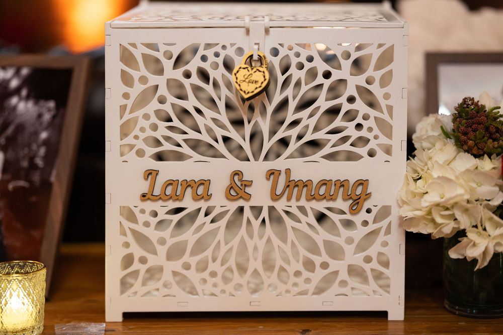 White laser-cut wedding card box engraved with Lara & Umang names, featuring intricate floral pattern design.