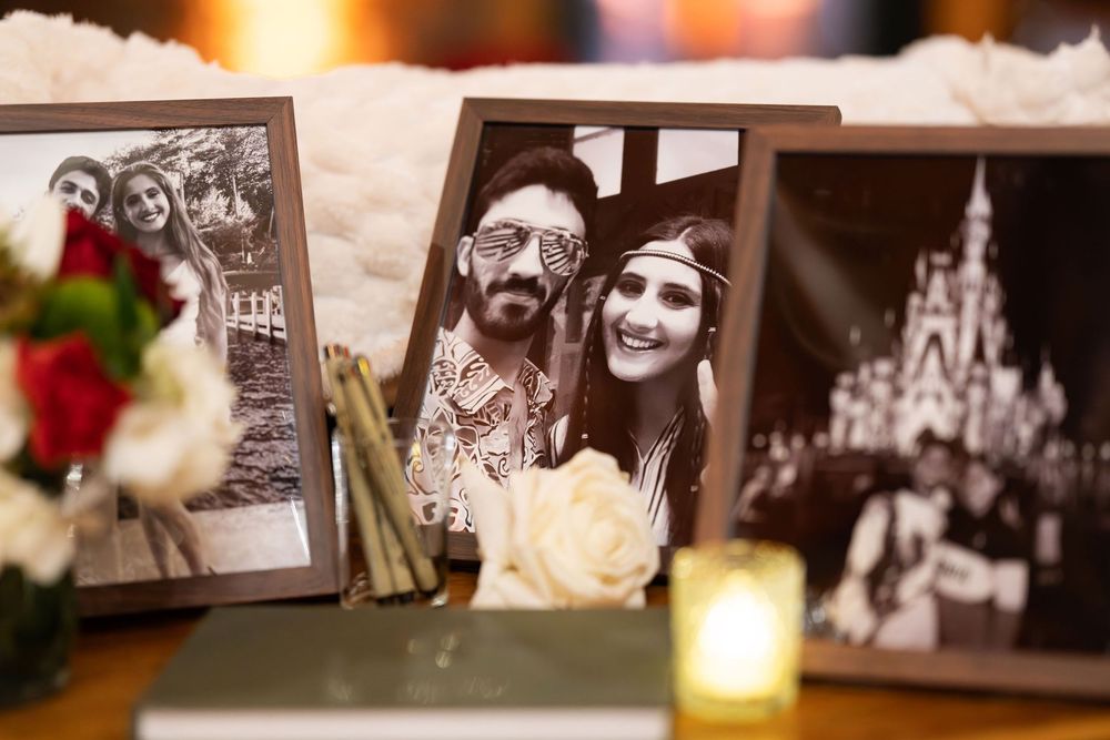 Framed black and white photos of couples displayed on a table with roses and candles at a wedding reception.