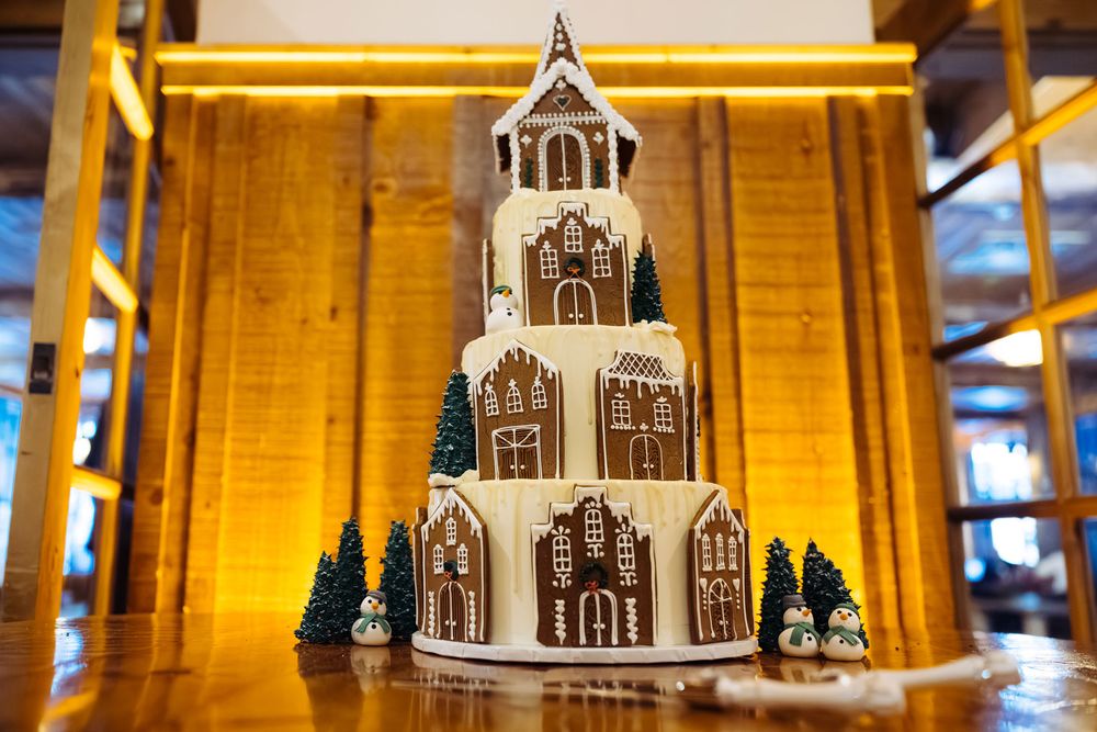 Multi-tiered wedding cake decorated with gingerbread houses and Christmas trees, perfect for a winter holiday celebration.