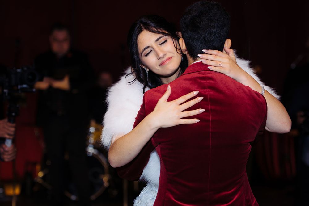 Two women share a warm embrace while dancing at a formal event, one wearing a white fur-trimmed dress.