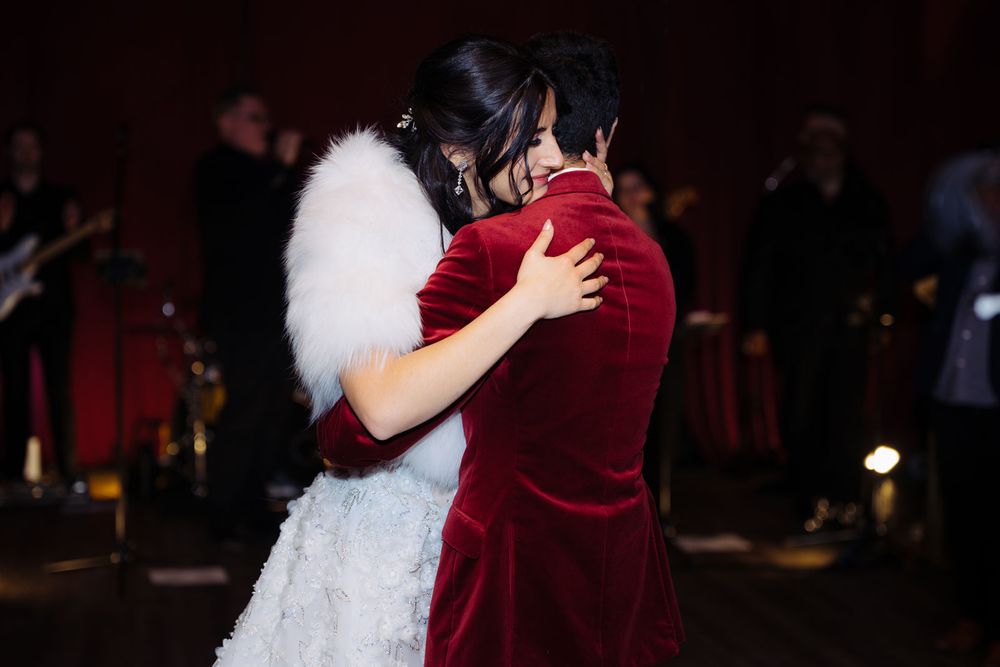 Two people share an emotional dance embrace at a wedding reception, one wearing a white fur stole.