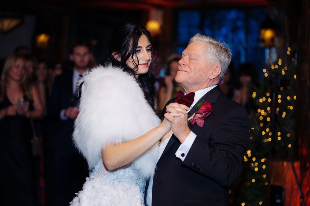 Elegant couple dancing at a formal wedding reception, woman in white feathered dress, man in tuxedo with red boutonniere.