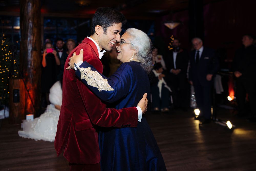 Groom in red velvet tuxedo shares a tender mother-son dance at an elegant wedding reception.